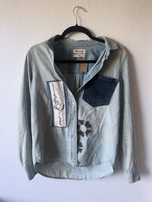 Light blue denim jacket with embroidered designs on a hanger against a white wall
